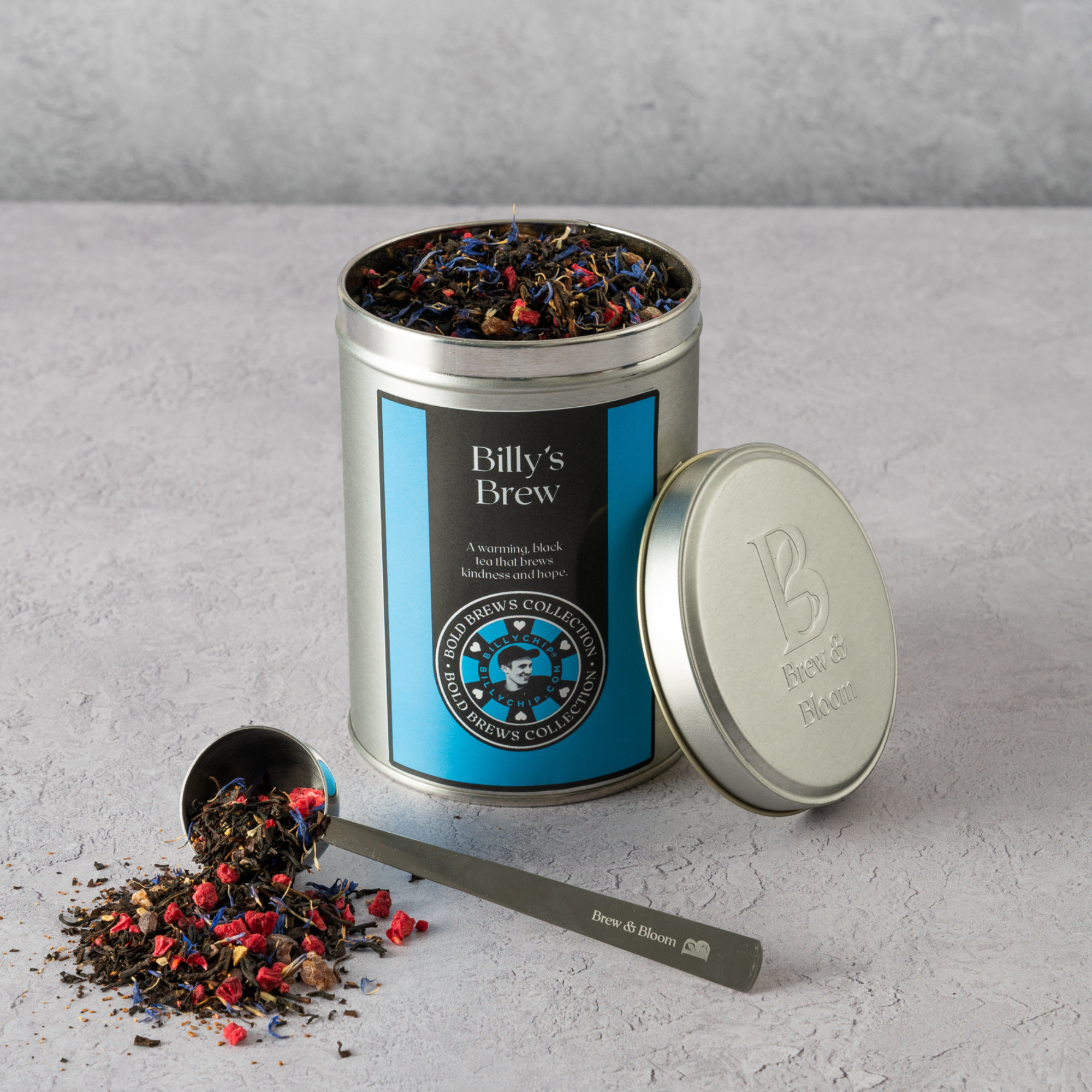 Tea canister labeled 'Billy's Brew' with tea leaves spilling out on a gray surface.