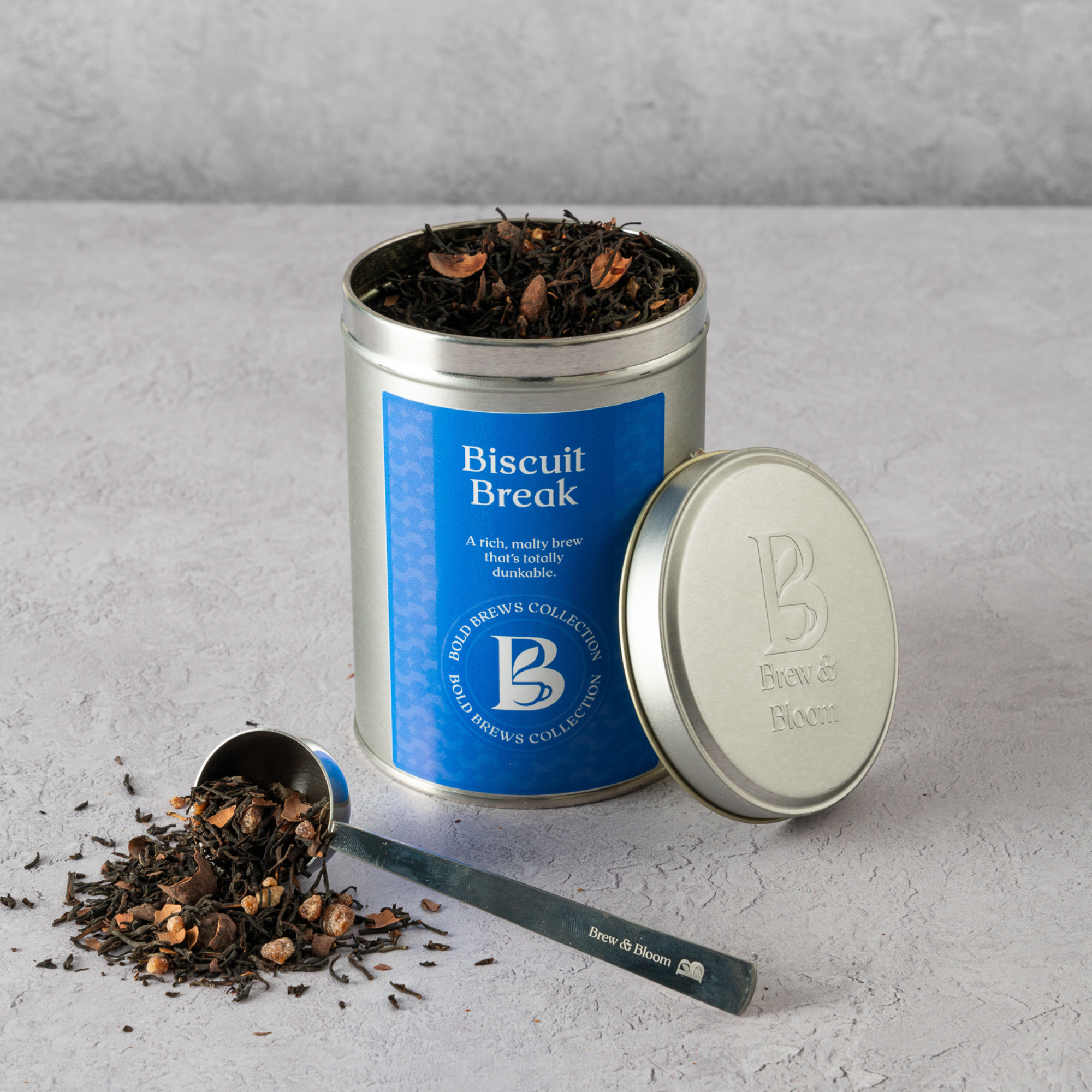 Tea canister labeled 'Biscuit Break' with tea leaves spilling out on a gray surface.