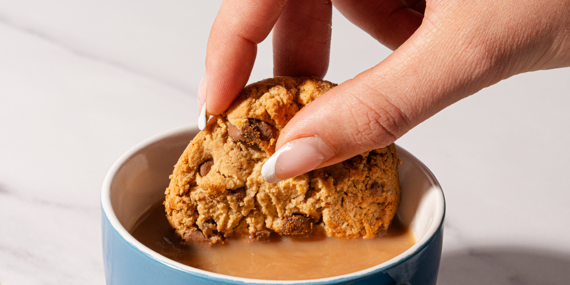 Chocolate chip biscuit being dunked into a cup of Brew & Bloom tea