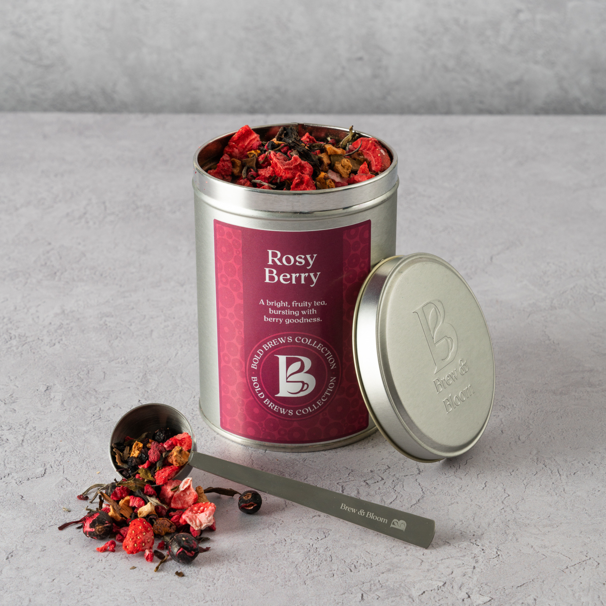Rosy Berry loose leaf white tea in Brew & Bloom tin with berry pieces and measuring spoon on stone background